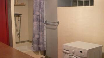 A laundry room with a washing machine, a shower, and a small window.
