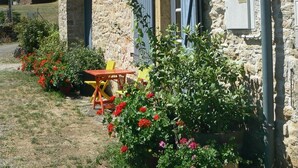 A stone building with a wooden table and chairs outside, surrounded by potted plants and flowers.