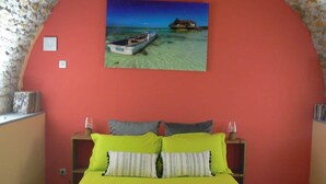 A bedroom with a bed, pillows, a nightstand, a lamp, and a painting of a beach scene.