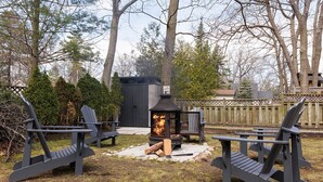 Un espace extérieur aménagé avec des chaises Adirondack et un poêle à bois.