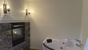 Un bagno moderno con camino in pietra, vasca freestanding e illuminazione a parete.
