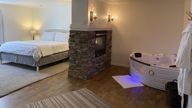 Una camera da letto con un camino in pietra, un letto con copriletto bianco, un comodino con lampada e una vasca da bagno bianca con asciugamano.