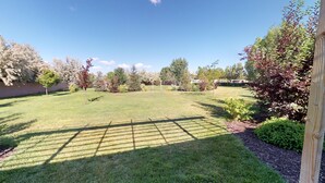 Un giardino curato con prato, una pergola in legno e diversi arbusti e alberi.