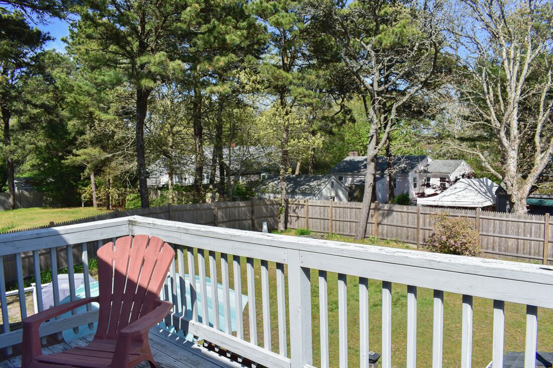 A wooden deck with a red Adirondack chair, surrounded by a white picket fence and trees.