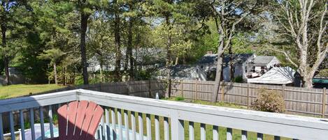 A wooden deck with a red Adirondack chair, surrounded by a white picket fence and trees.