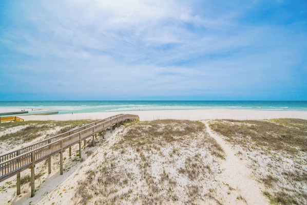 A beach with a wooden boardwalk leading to the water, sandy dunes, and a clear sky.
