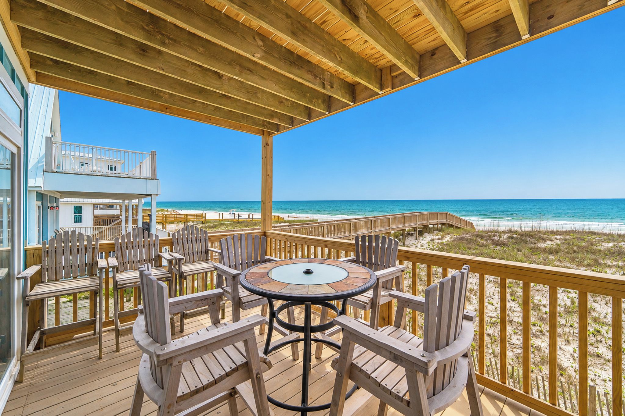 A wooden deck with a table and chairs overlooking a beach.