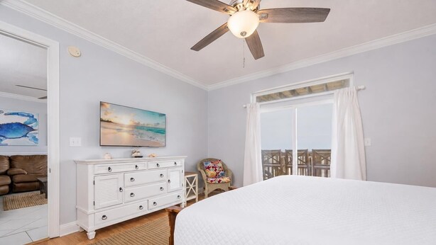 Une chambre à coucher comprenant un lit, une commode, une chaise, un ventilateur de plafond, une télévision et une grande fenêtre.