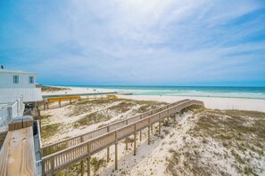 A beach view with a wooden boardwalk, a beach house, and a sandy beach.