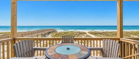 A wooden deck with a round table and chairs, overlooking a beach with a wooden walkway.