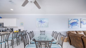 Un coin repas avec une table à plateau en verre, des chaises à rayures, un ventilateur de plafond et des œuvres d’art accrochées au mur.