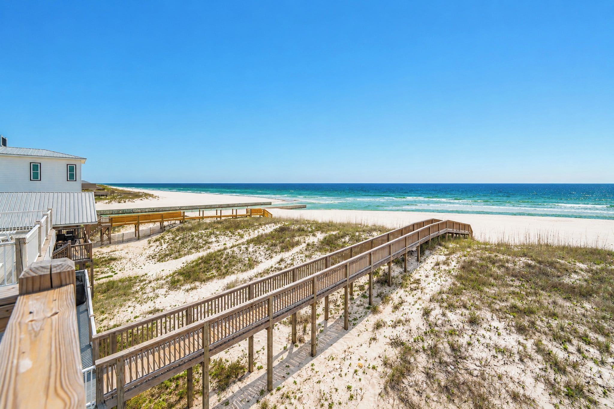A beach with a wooden boardwalk leading to a white building with a metal roof.