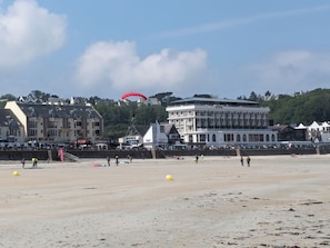 A beach with buildings in the background, including a white building with balconies.