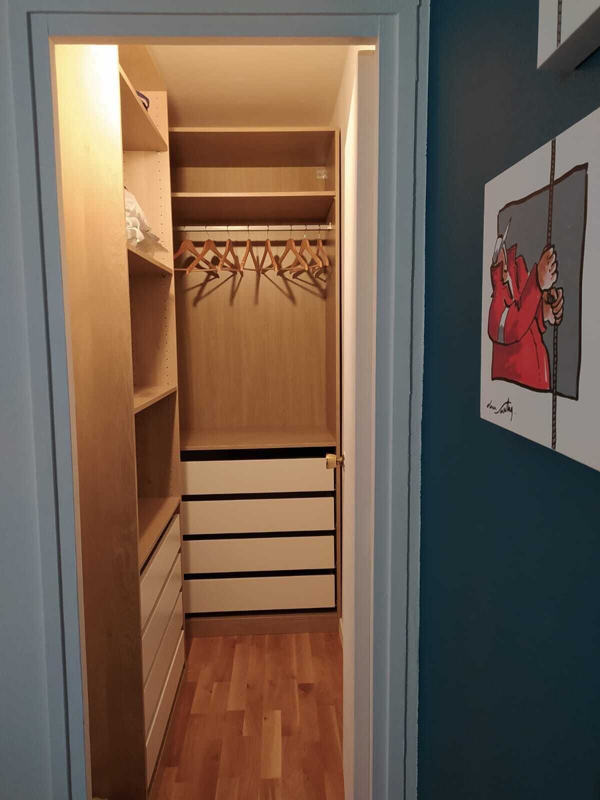 A walk-in closet with wooden shelves and a hanging rod, a wooden floor, and a door with a brass handle.