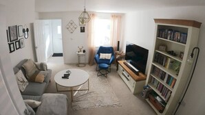 Una sala de estar con un sofá, una mesa de centro, un sillón azul, un televisor y una estantería.