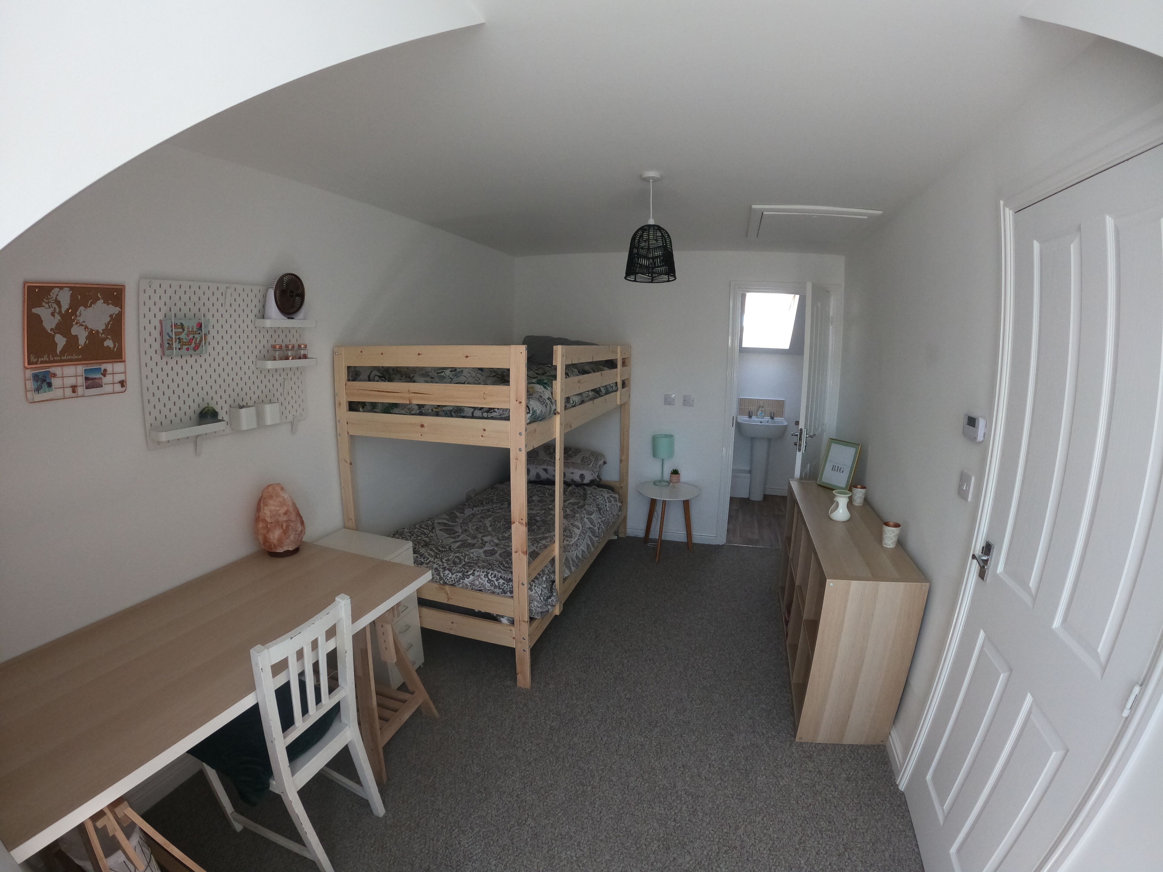 Et værelse med køjesenge, et skrivebord, en stol, et lille bord, en lampe, en vask og en dør.