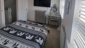 Un dormitorio con cama, cómoda, tocador y televisor en la pared.