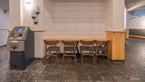 A corner seating area with a wooden table and four chairs, a payment kiosk, and a wall-mounted light fixture.
