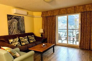A living room with a brown leather sofa, a wooden coffee table, and a large painting on the wall. - Spectacular 1 BR Suite - Family-friendly/Gym/BBQ/AC (Canmore)