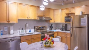A modern kitchen with wooden cabinets, stainless steel appliances, a marble countertop, and a dining area with a round table and white chairs.