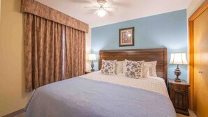 A hotel room with a large bed, wooden headboard, two bedside lamps, a ceiling fan, and a framed picture on the wall.