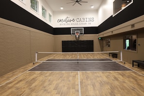 An indoor sports court with a basketball hoop, wooden flooring, and a ceiling fan. - L3nee's Lay-Up by Creative Cabins (Logan)