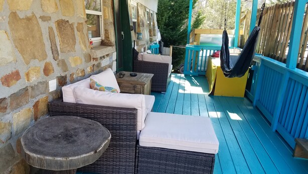 A covered outdoor seating area with wicker furniture and cushions, a hammock, and a stone wall backdrop.