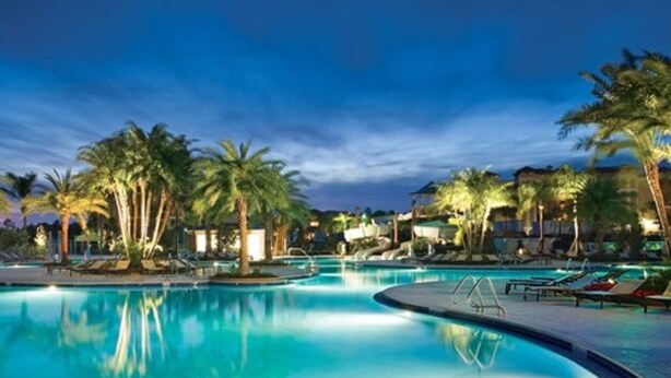 A large outdoor swimming pool surrounded by palm trees and lounge chairs, with buildings in the background. - Three Bedroom Deluxe Condo, Orlando, Florida (2194699) (orlando)