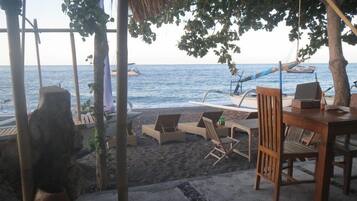 A beachside seating area with lounge chairs and a table, overlooking the sea.
