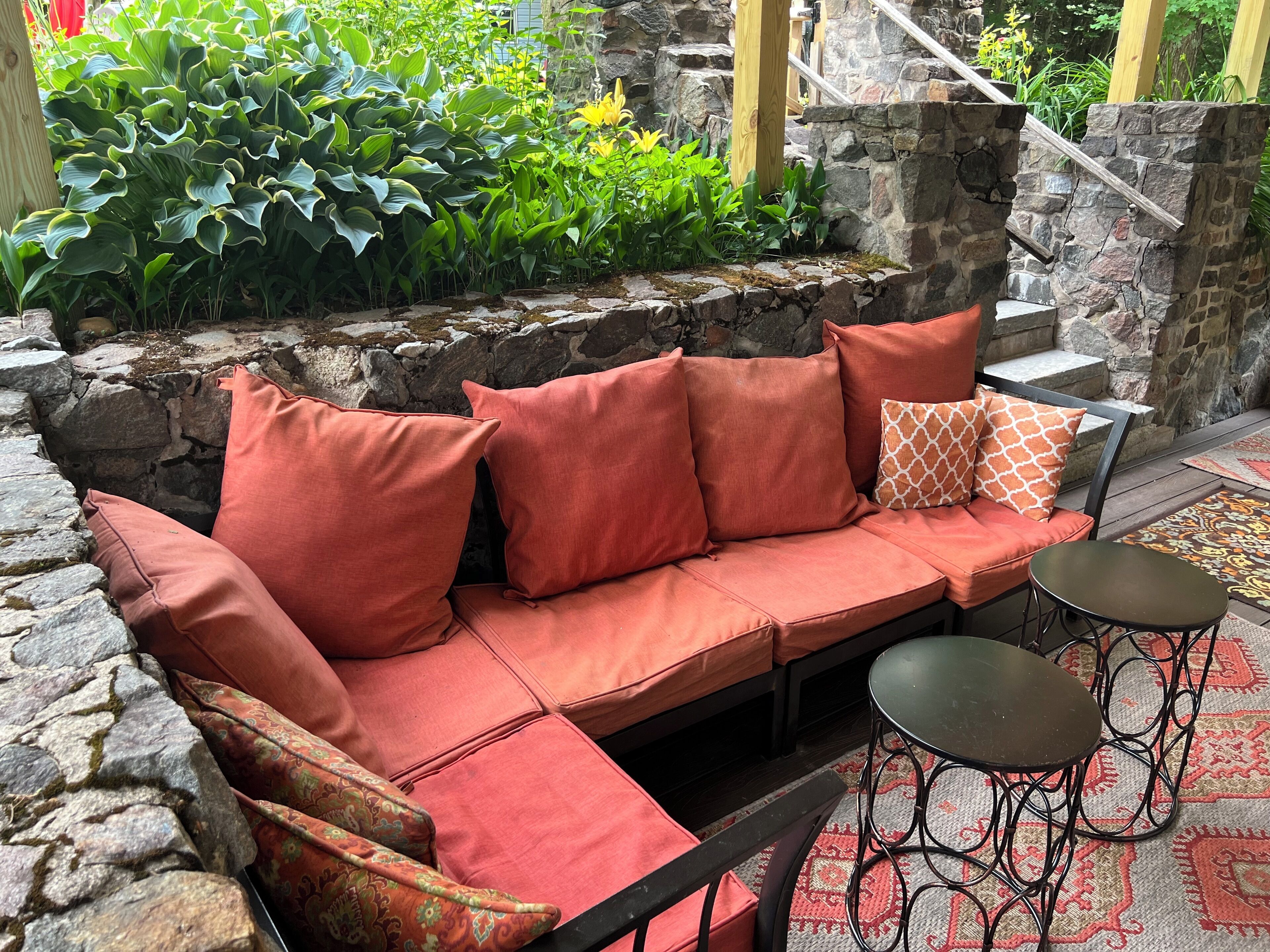 A stone-walled outdoor seating area with a cushioned sofa and two small tables.