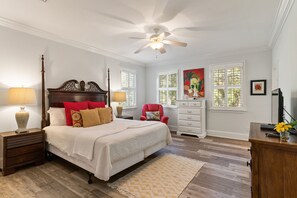 Une chambre à coucher avec un grand lit, deux tables de chevet, un ventilateur de plafond et une commode.