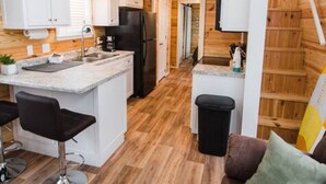 A compact kitchen with white cabinets, a black refrigerator, and a wooden floor.