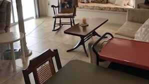 A living room with a sofa, a rocking chair, a table, and a window with curtains. - Le Beau Soleil (Sun City West)