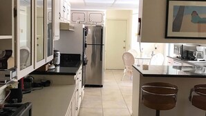 A modern kitchen with a central island, stainless steel appliances, and a dining area with white chairs. - Le Beau Soleil (Sun City West)