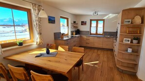 A cozy kitchen with wooden cabinets, a dining table, and a view of mountains through the window. - Apartment Hipp No. 3 - 90m² new building on the 1st floor with balcony and mountain view in a top location (Halblech)