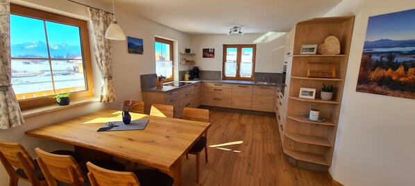 A cozy kitchen with wooden cabinets, a dining table, and a view of mountains through the window.