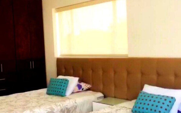 A bedroom with a large window, a tufted headboard, two beds, and a wardrobe.