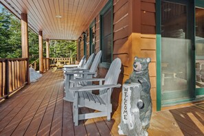 A wooden deck with Adirondack chairs and a bear statue.