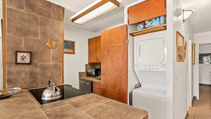 Une cuisine moderne équipée d’une cuisinière, d’un four à micro-ondes et d’un lave-vaisselle. On y trouve un meuble en bois, avec un four à micro-ondes posé sur le dessus et un lave-linge dans un coin.