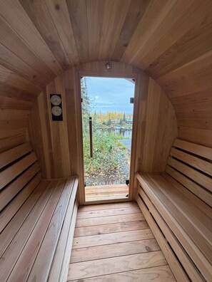 A sauna with wooden walls and benches, a view of a lake, and a thermometer on the wall.
