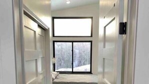 A narrow hallway leading to a room with a bed and a large window.