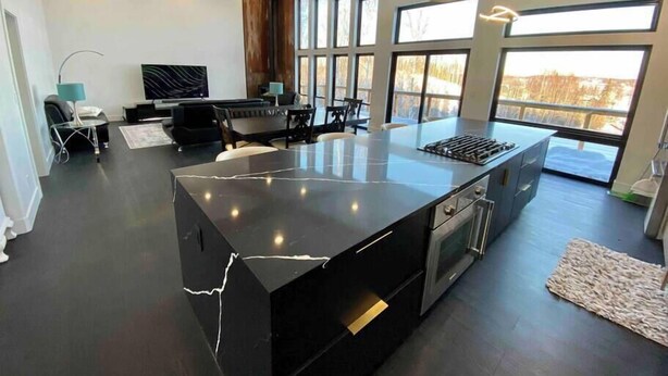 A modern kitchen with a large island, built-in oven, and a dining area with a bench and table.