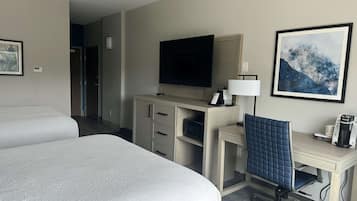 Een hotelkamer met twee bedden, een bureau met stoel, een televisie, een koffiezetapparaat en een lijst aan de muur.