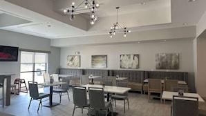 A modern dining area with a high ceiling, pendant lighting, and a mix of seating options including tables and a bench. - Best Western Plus Chandler (Chandler)