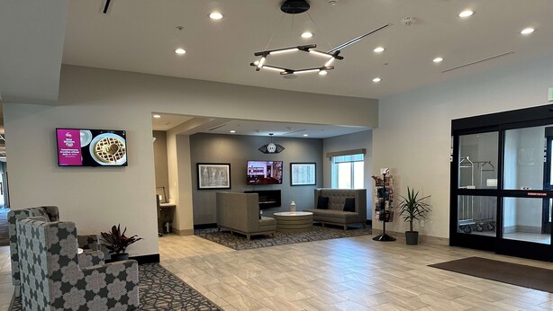 A hotel lobby with a modern design, featuring a seating area with sofas and armchairs, a coffee table, and a patterned rug. There is a television mounted on the wall, a framed artwork, and a plant in the corner. - Best Western Plus Chandler (Chandler)
