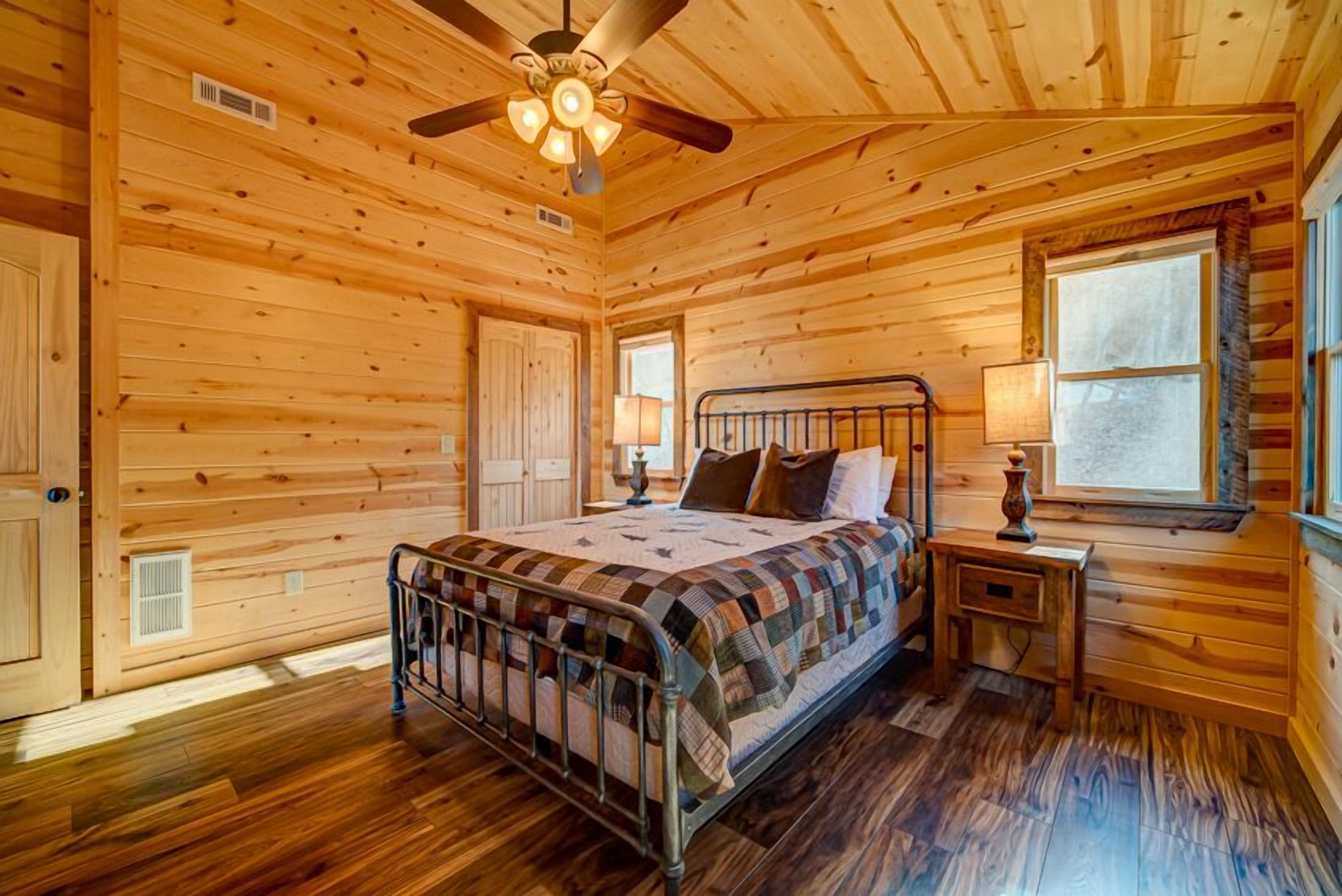Ein Schlafzimmer einer Holzhütte mit einem Metallbett, einem Deckenventilator und einem Fenster mit Blick.