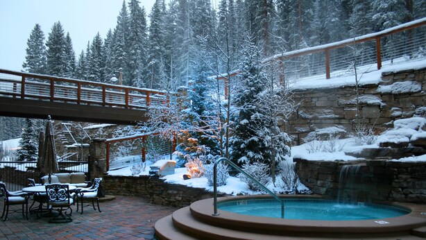 A snow-covered outdoor area with a hot tub, patio furniture, and a stone wall. - Timbers 3076 (Keystone)