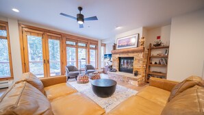 A spacious living room with leather sofas, a stone fireplace, and large windows offering a view of trees. - Timbers 3076 (Keystone)