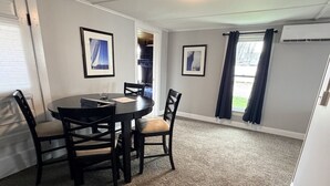 A dining area with a round table and four chairs, a carpeted floor, and framed pictures on the walls. - Walk to Lake • Strip • Wineries • Firepit (Geneva)