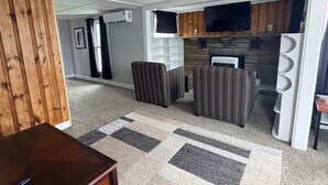 A living room with a fireplace, striped sofas, a wooden cabinet, and a TV. - Walk to Lake • Strip • Wineries • Firepit (Geneva)